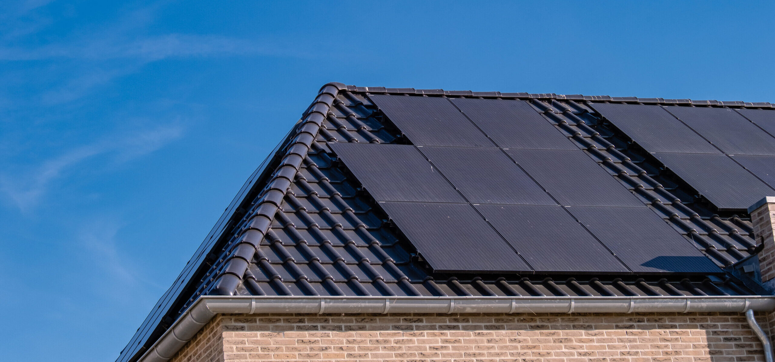 Newly build houses with solar panels attached on the roof against a sunny sky Close up of new building with black solar panels. Zonnepanelen, Zonne energie, Translation: Solar panel, , Sun Energy.